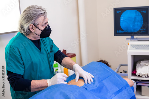 Doctor practices the infiltration of drugs to the patient in the area affected by the pain, using the ultrasound support to visualize the anatomical components of the spine.