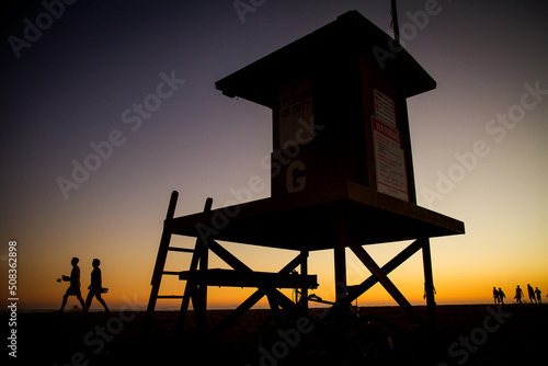 Silhouette of people around a lifeguard tower at sunset