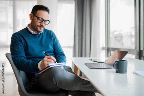 Confident entrepreneur making business plan in diary while working at office