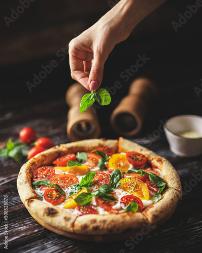 Appetizing pizza with tomatoes and cheese on a dark wooden background. Slice of pizza with stretchy cheese