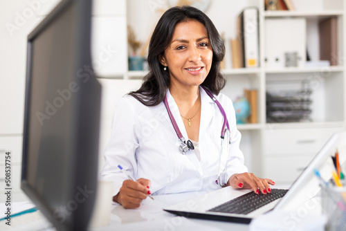 Portrait of smiling Colombian woman physician consulting patient in medical office