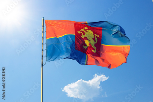 Wind waving the flag of Krasnoyarsk against the background of a blue sky with sun