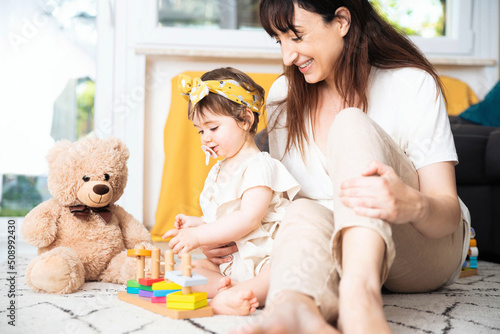 Mother and kid girl playing educational toys together in living room - Mom and daughter doing activities together at home - Happy family and babysitting concept