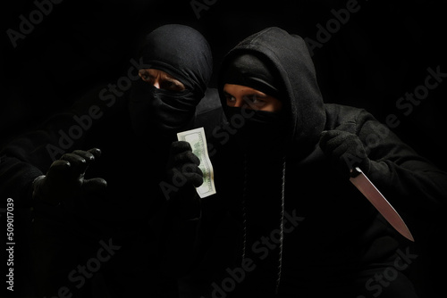 thieves in black masks with a knife and dollars in their hands on a black background. robbers in black balaclava with a knife and dollars in their hands. terrorists in masks. 