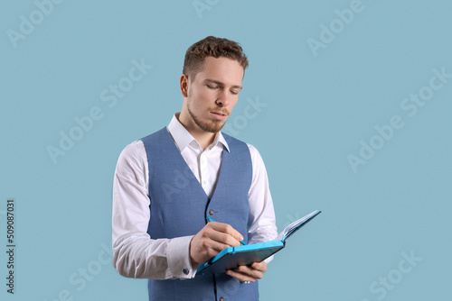 Portrait young man in business suit on blue background with an open notebook in his hands. Makes notes in a notebook. Caucasian guy office worker
