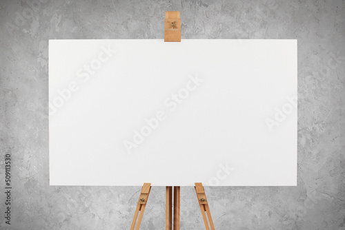 A blank artist's canvas on an easel against a concrete wall background. 