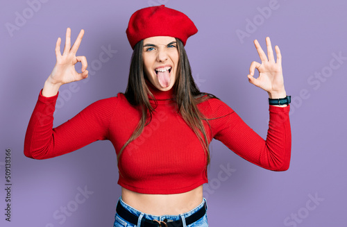 Young brunette teenager doing excellent gesture with hand sticking tongue out happy with funny expression.