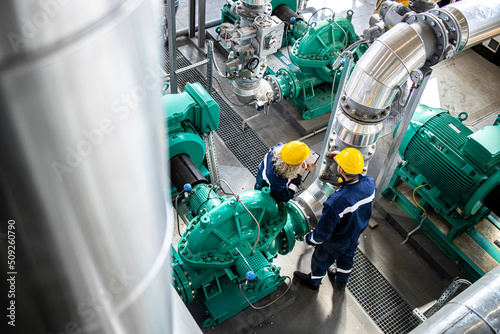 Industrial workers or serviceman standing on refinery platform checking gas pipes and engine generators.