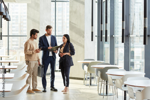 Minimal full length portrait of three business people talking in graphic white interior of office building, copy space