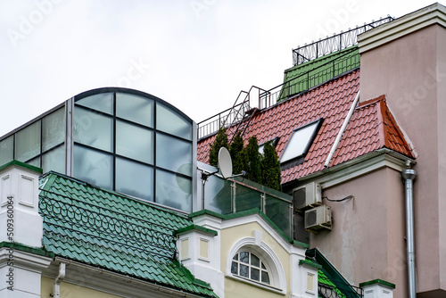 Glazed conservatory garden on terrace with thuja and red roof with skilight windows, gutters and drainpipes of city residential house
