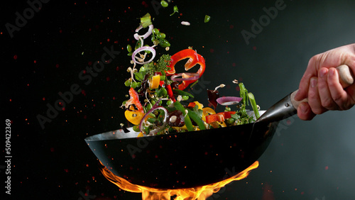 Closeup of chef throwing vegetable mix from wok pan in fire.