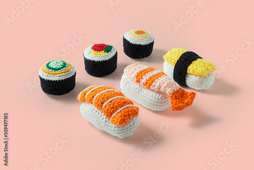 Assorted set of maki sushi rolls and nigiri sushi handmade in crochet and colored wool. Sushi set isolated on a pink background. Sushi crochet amigurumi