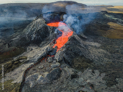 Volcanic landscape on Iceland's Reykjanes peninsula. View of the crater from above. Liquid lava flows out. Steam and smoke near the crater. cooled magma around craters