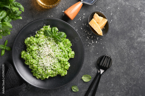 Italian risotto. Delicious risotto with pesto sauce or wild garlic pesto, basil, parmesan cheese and glass of white wine on dark slate table background. Italian dinner. Top view with copy space.