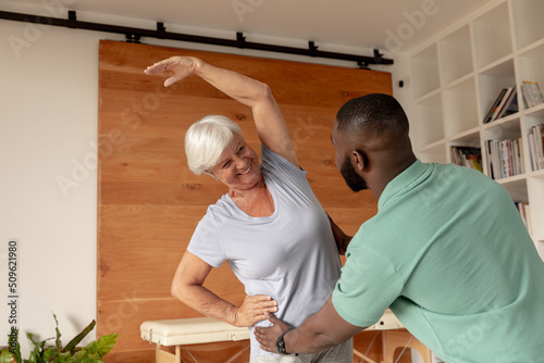 African american male physiotherapist helping caucasian senior woman to perform stretching exercise