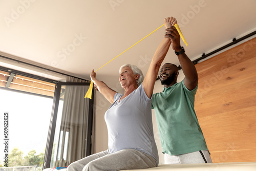 African american male physiotherapist helping senior woman to exercise with resistance bands