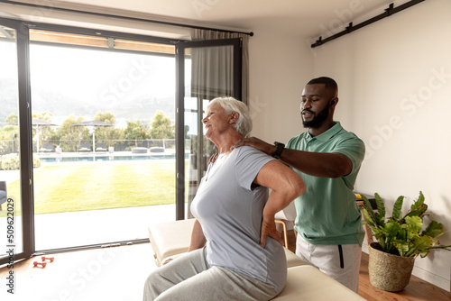 African american male physiotherapist massaging neck of caucasian senior woman at home