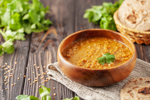 Indian dal food (Masoor Dal or Dal Tadka Curry) and homemade Flatbread Chapati. Traditional Indian soup lentils. Indian Dhal spicy curry in bowl, spices, herbs, rustic black wooden background.