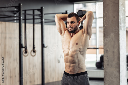 Athletic man with a naked torso trains his triceps with dumbbells in his hands. Workout in the gym. Bodybuilding and fitness, healthy lifestyle