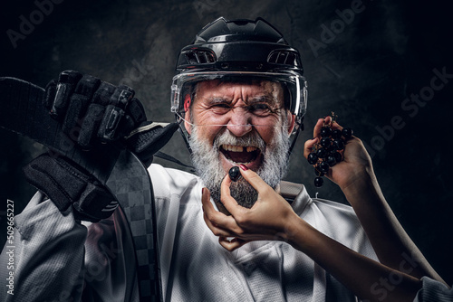 Shot of angry hockey player being fed with grape by woman against dark background.