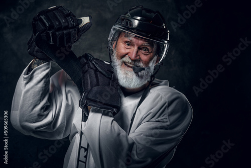 Studio shot of happy gray haired grandfather hockey player dressed in white sportswear.
