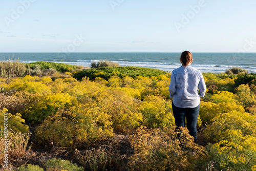 Mujer de espaldas, entre la vegetación, observando la playa de la ballena en la provincia de Cádiz, España, foto tomada el 4 de julio de 2022