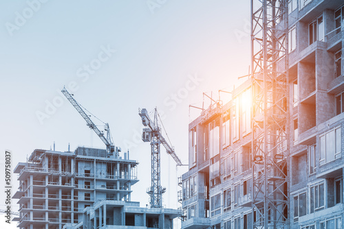 Modern apartment residential building glass facade wall construction site with many high tower cranes and heavy machinery against blue sky background. Industrial scenic urban city development project