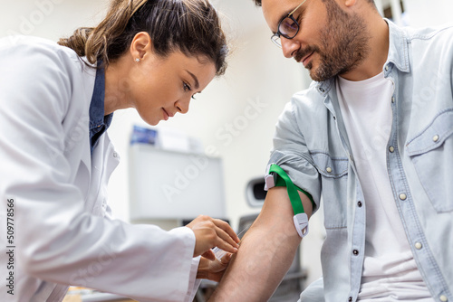 Friendly hospital phlebotomist collecting blood sample from patient in lab. Preparation for blood test by female doctor medical uniform on the table in white bright room