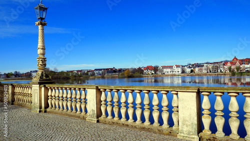 weiße Balustrade mit Laterne entlang des Burgsees vor dem Schweriner Schloss unter blauem Himmel