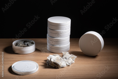 Studio shot of white swedish smokeless tobacco cans and portion snus pouches on a wooden table.