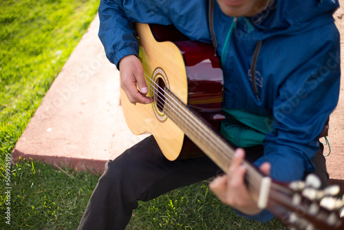 Detalle de joven cantando y tocando guitarra en un parque al atardecer. Concepto de personas y música.
