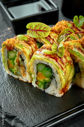 Vegetarian sushi rolls with avocado, mango and sauces isolated on a black plate. Close-up