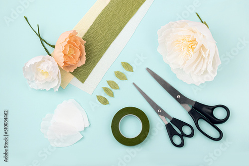 Hand made crepe paper flowers, leaves, scissors and floral tape flat lay. Paper peony DIY concept
