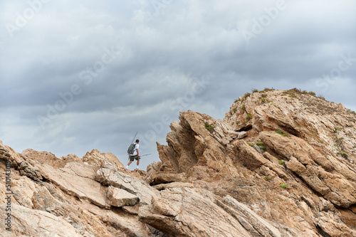 Young man carrying a backpack with sport fishing equipment goes to a fishing point hiking in Rodos Islet, Portman, Murcia coast. Spinning mode fisherman.