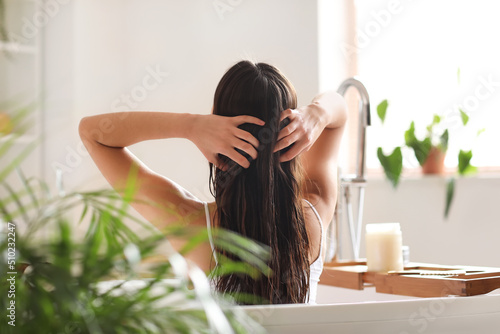 Young woman applying coconut oil onto her hair in bathroom