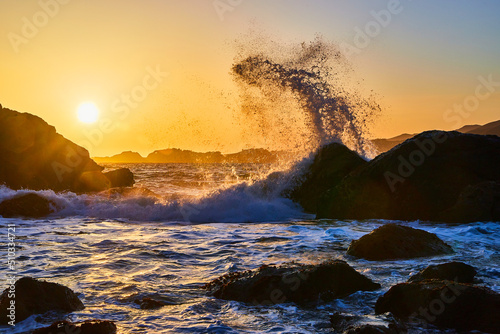 Stunning splash of ocean waves off large rocks at sunset