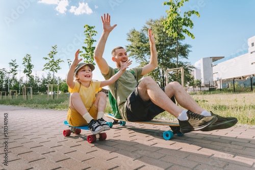 Happy father and his daughter riding sitting on skateboards outdoor