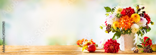 Autumn still life with garden flowers. Beautiful autumnal bouquet in vase, apples and berries on wooden table. Colorful dahlia and chrysanthemum.