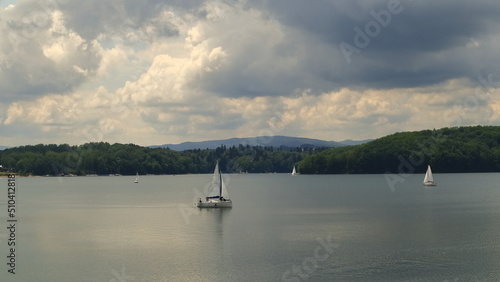 A white sailboat on the Soliński lake. Dark leaden clouds in the sky. Biała żaglówka na jeziorze Solińskim. Ciemne ołowiane chmury na niebie.