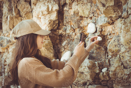 Teenage girl in cap photographing rocks with smartphone, monochromatic nude beige
