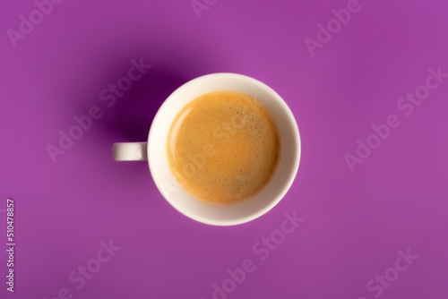 Minimalist food composition with morning aromatic americano coffee with foam on violet purple background from above. 