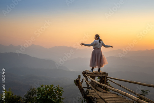 Woman standing and enjoying sunset on the mountain, Thailand.