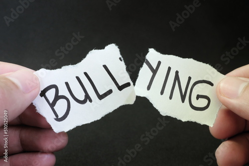 Fight and stop bullying concept. Hand tearing paper with word bullying in dark black background.