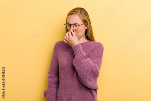 young adult blonde pretty woman feeling disgusted, holding nose to avoid smelling a foul and unpleasant stench