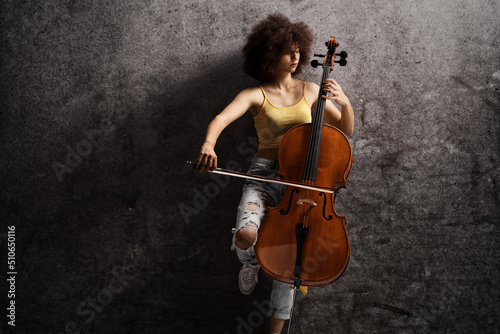Young female artist playing a cello and leaning on a rusty wall