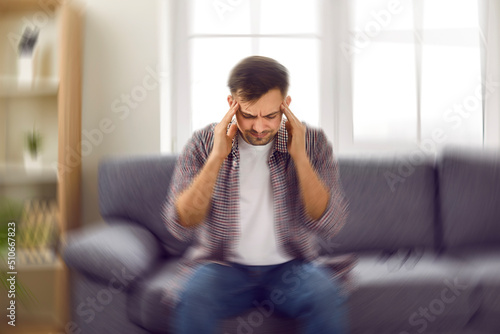 Man suddenly feels dizzy and takes a seat on the sofa. Young guy feeling pain and spinning sensation in his head. Headache, vertigo, health problem, brain tumor concept