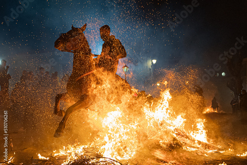 horses with their riders jumping bonfires as a tradition to purify animals..