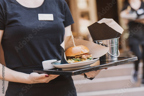The waiter takes the burger to the outdoor summer area in the cafe. street fast food