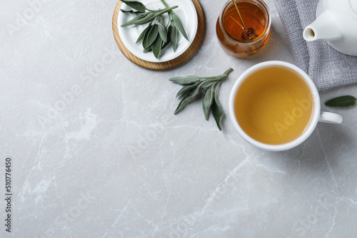 Flat lay composition with aromatic sage tea on light grey table. Space for text