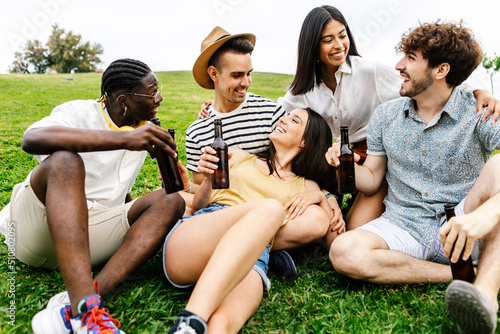 United group of millennial best friends hanging out relaxing on city park - Happy multiracial young friends cheering with beer while celebrating together on holidays